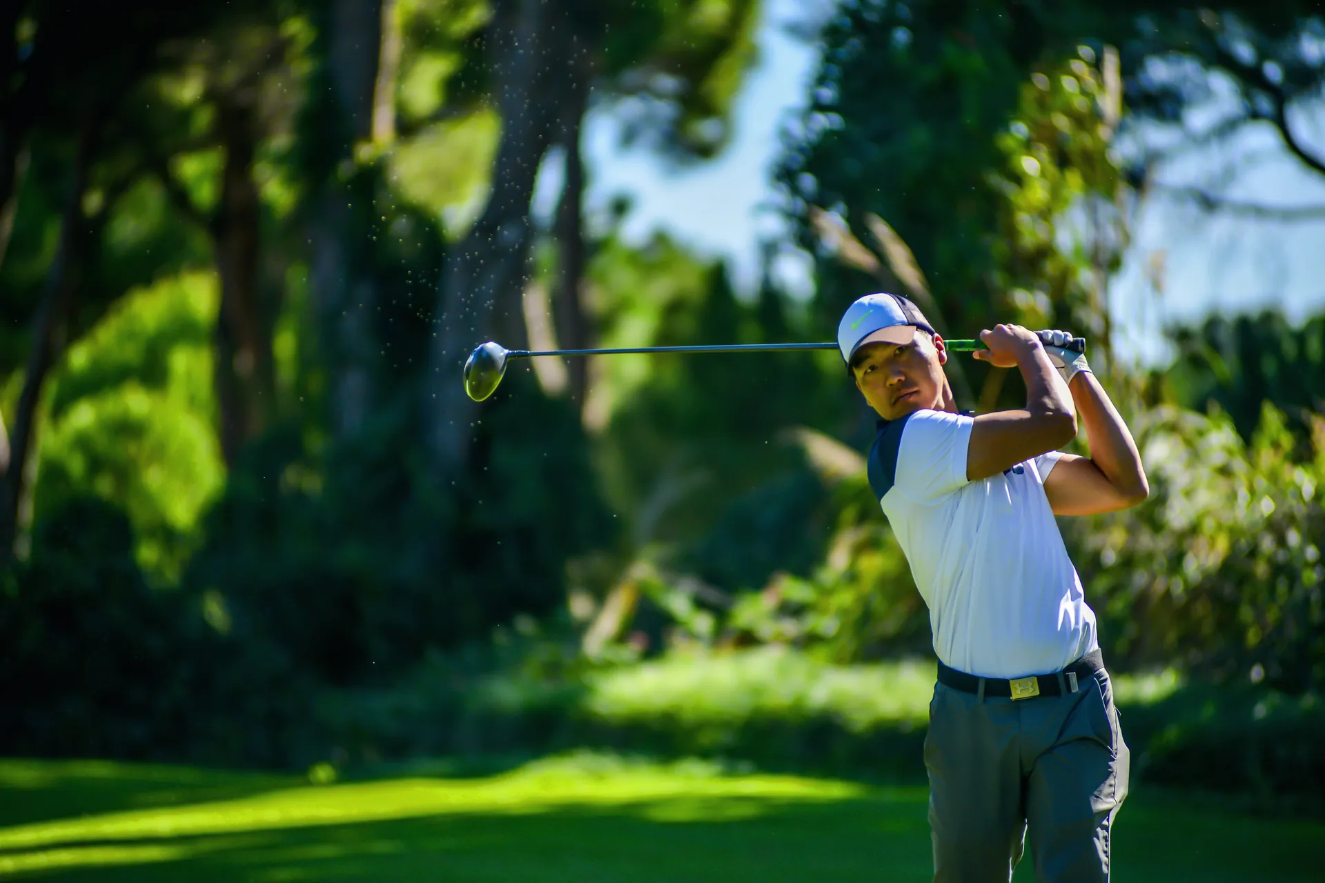 A golfer mid-swing on a tree-lined course.