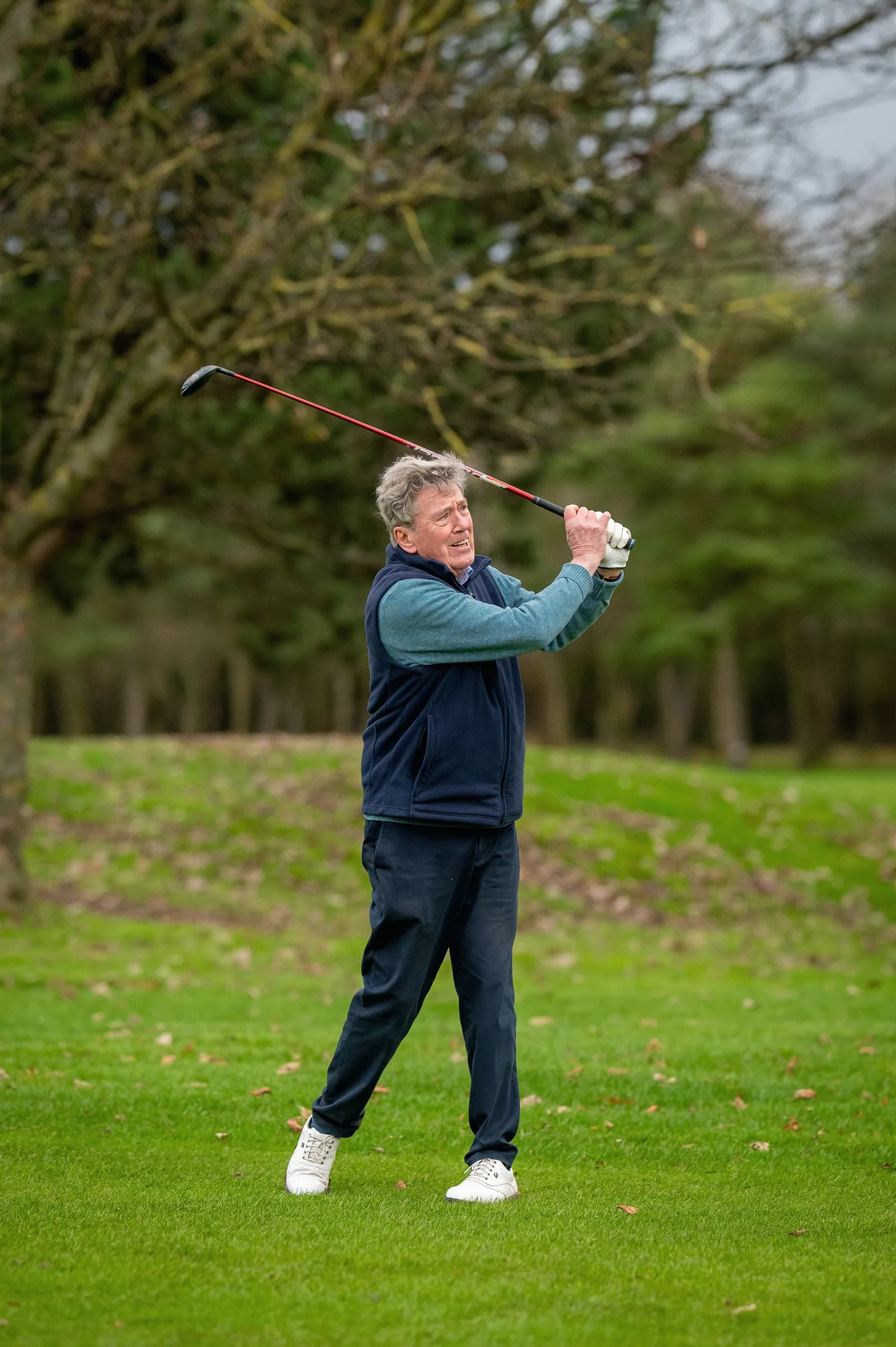 An older man swinging a golf club on a park lawn.