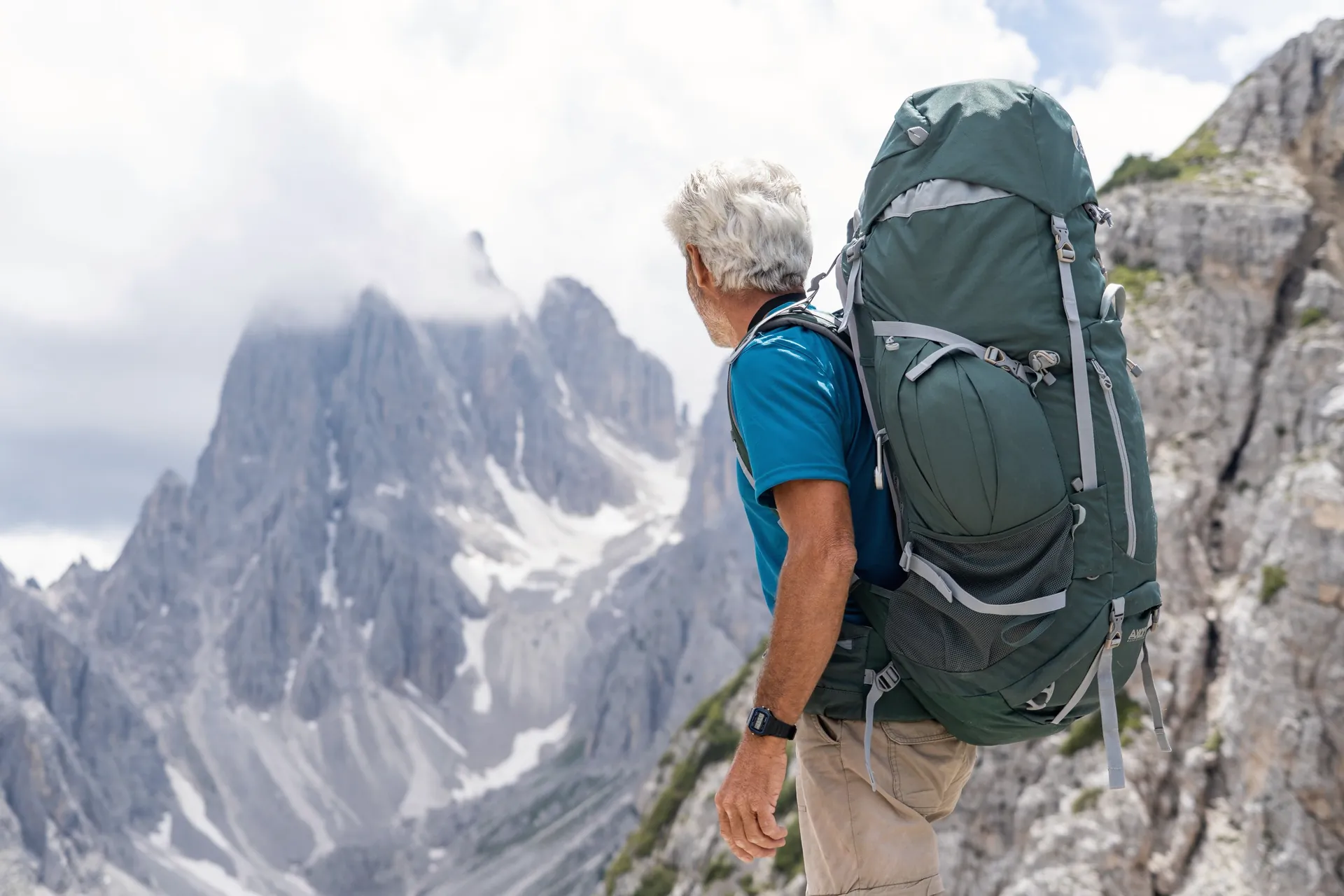 A grey-haired man with a rucksack looking out over mountain peaks.