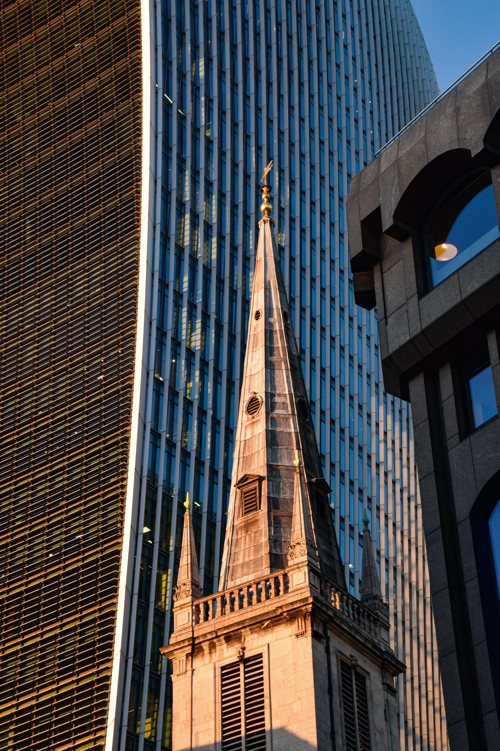 A church spire in front of glass towers in the City of London.